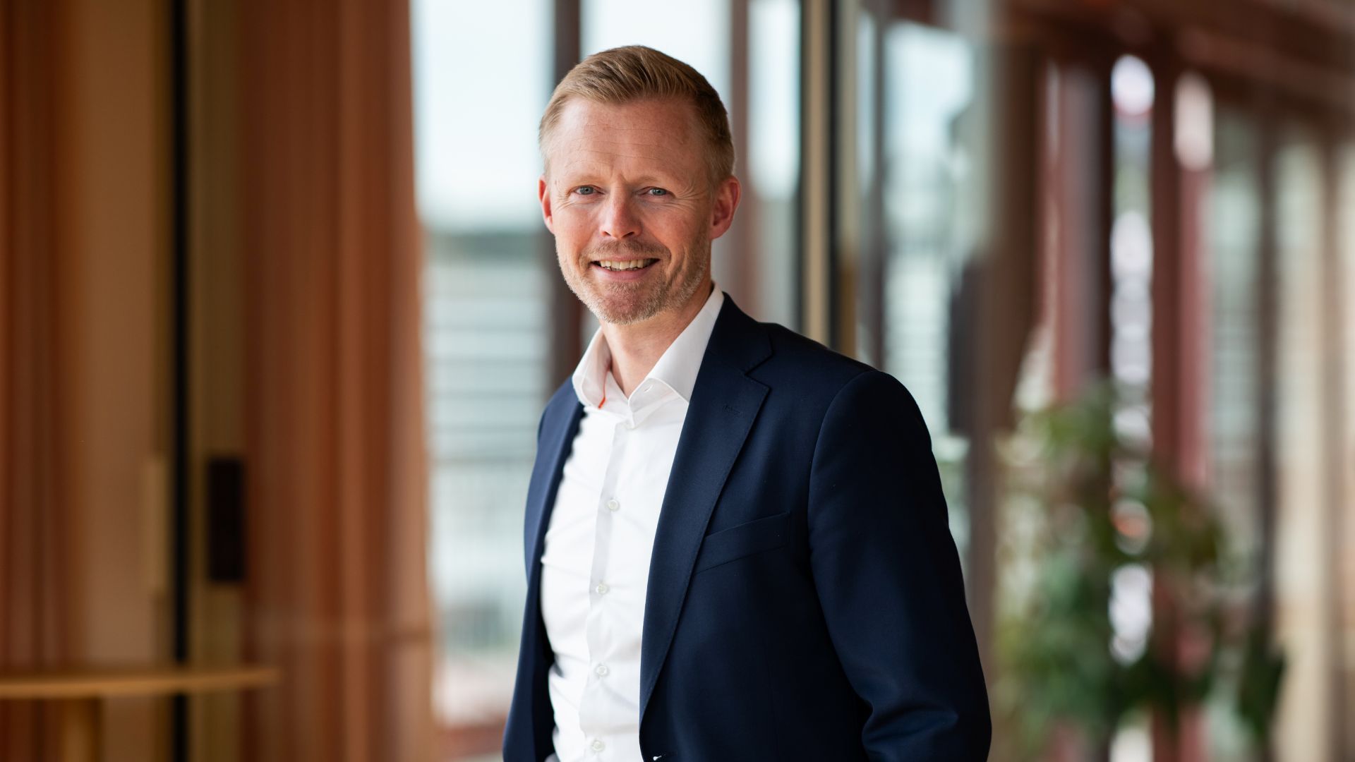 Kaare Wiik smiler til kamera i blå dress i et lyst og moderne lokale