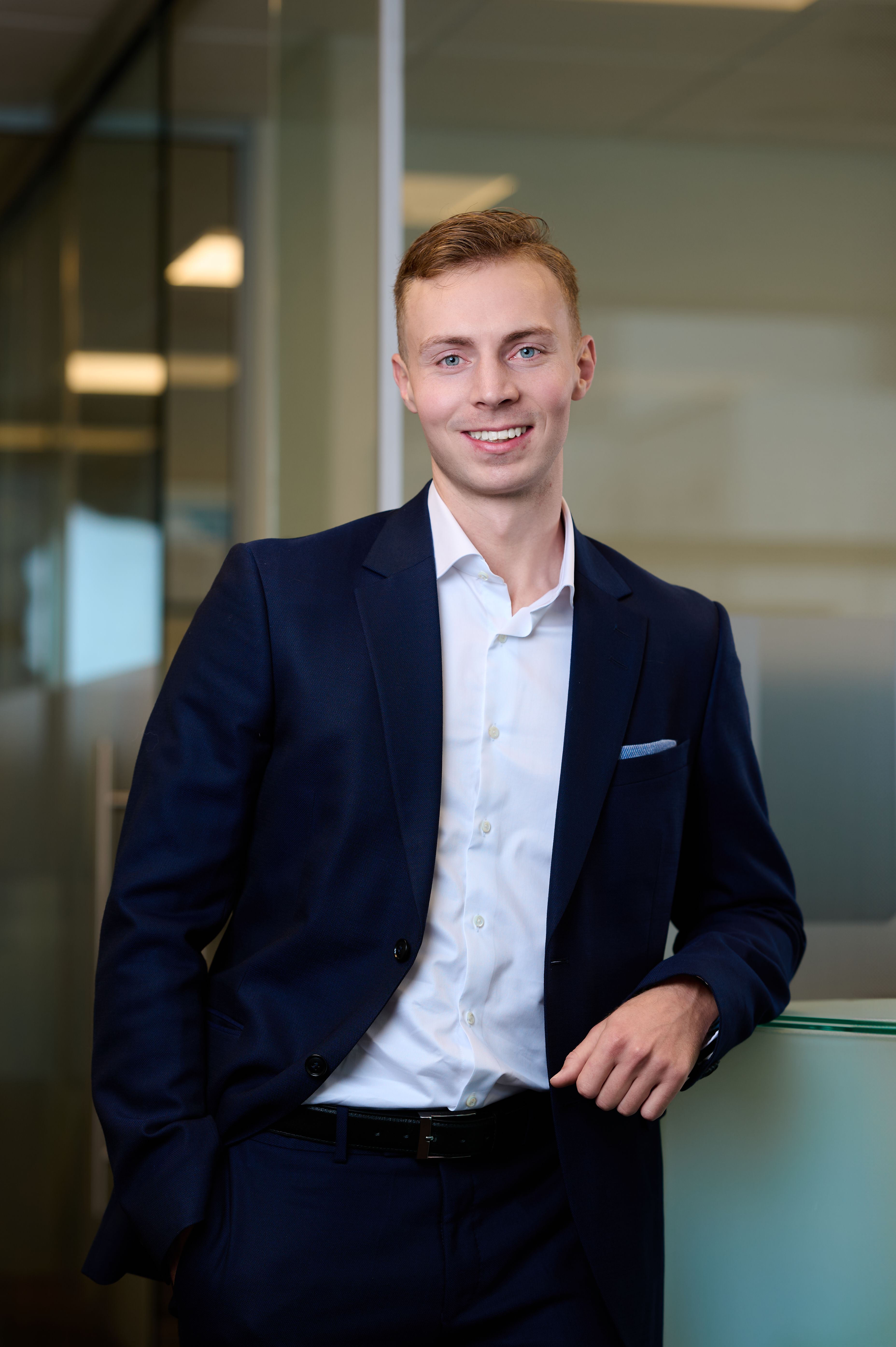 Mathias Aas bedriftsrådgiver i Kristiansund i blå dress i et moderne lokale som smiler til kamera