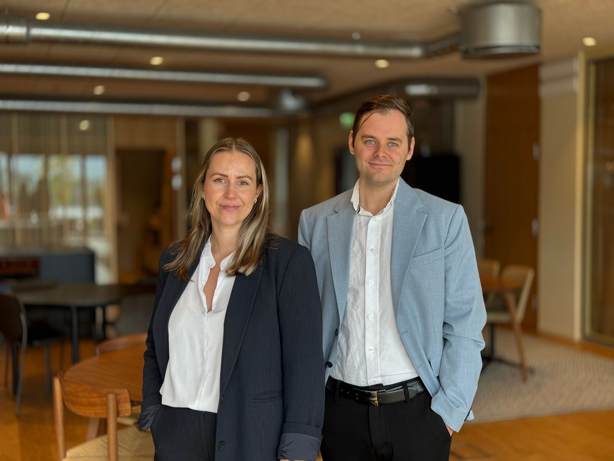 Mann og kvinne i dressjakke og hvit skjorte. Moderne kontorlokaler i bakgrunn 