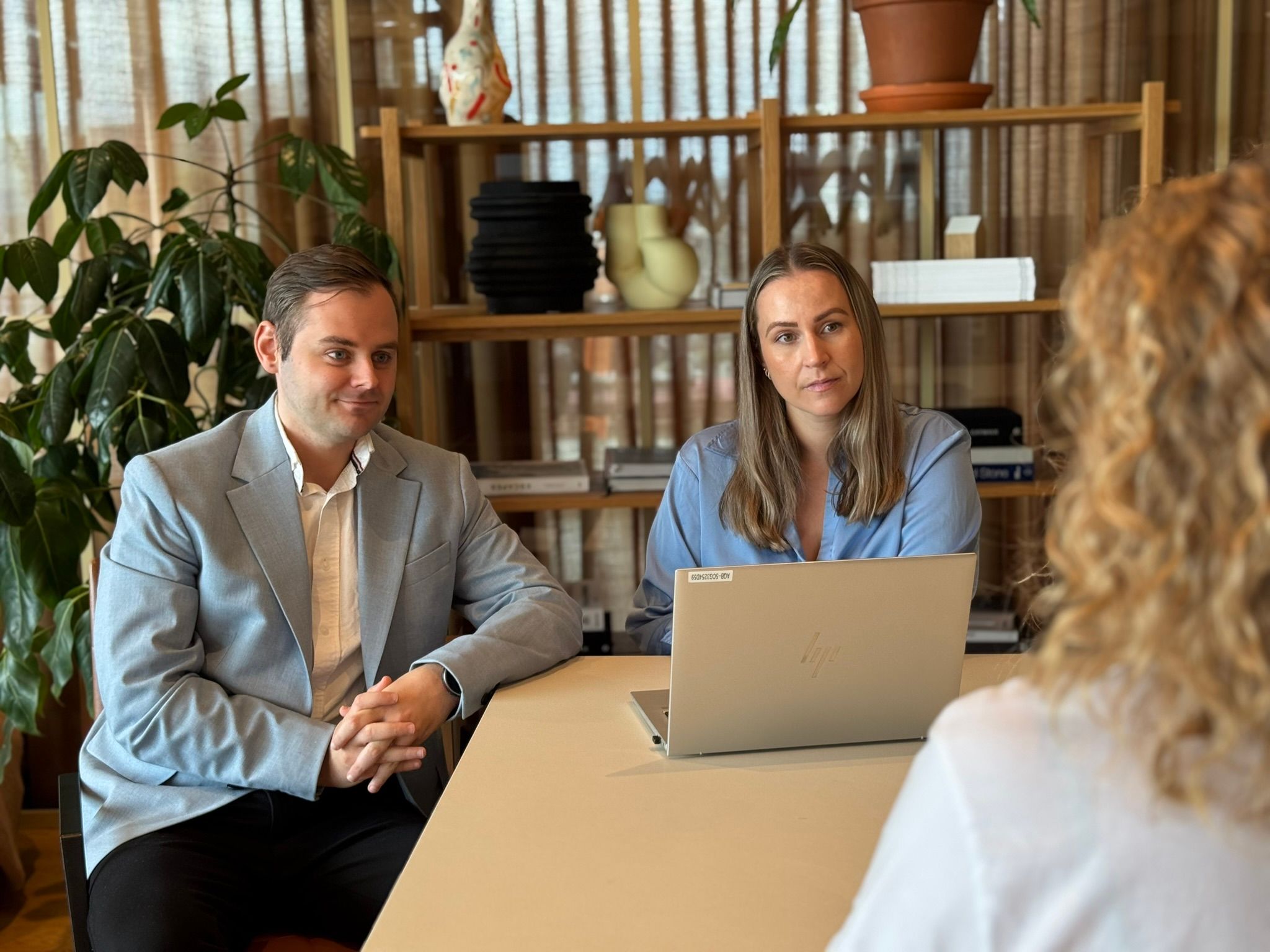 Mann og kvinner som sitter ved en bord med laptop mellom dem og en kvinne. Begge lytter til kvinnen. 