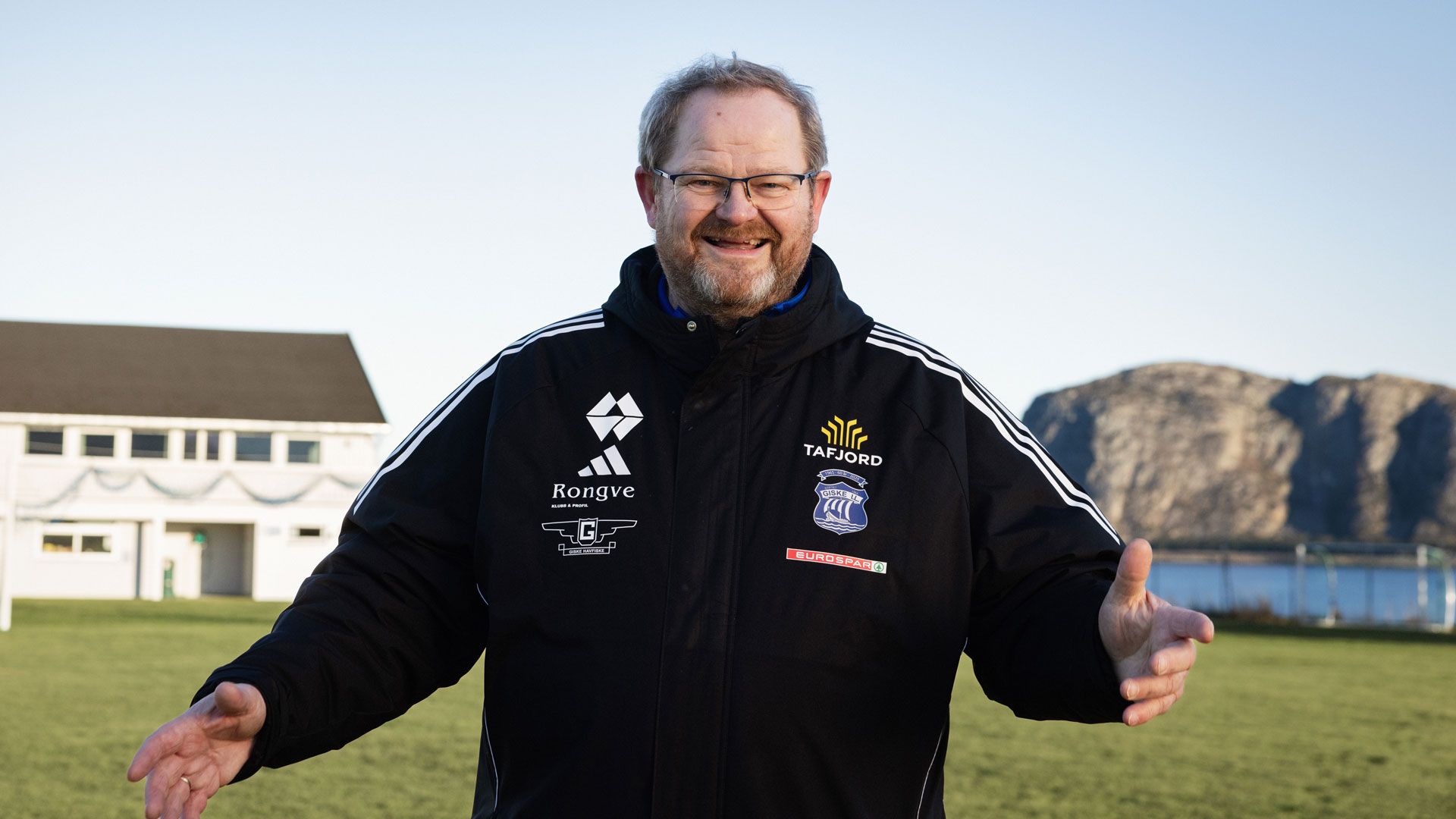 Mann står på en fotballbane. Smiler mot kamera. 