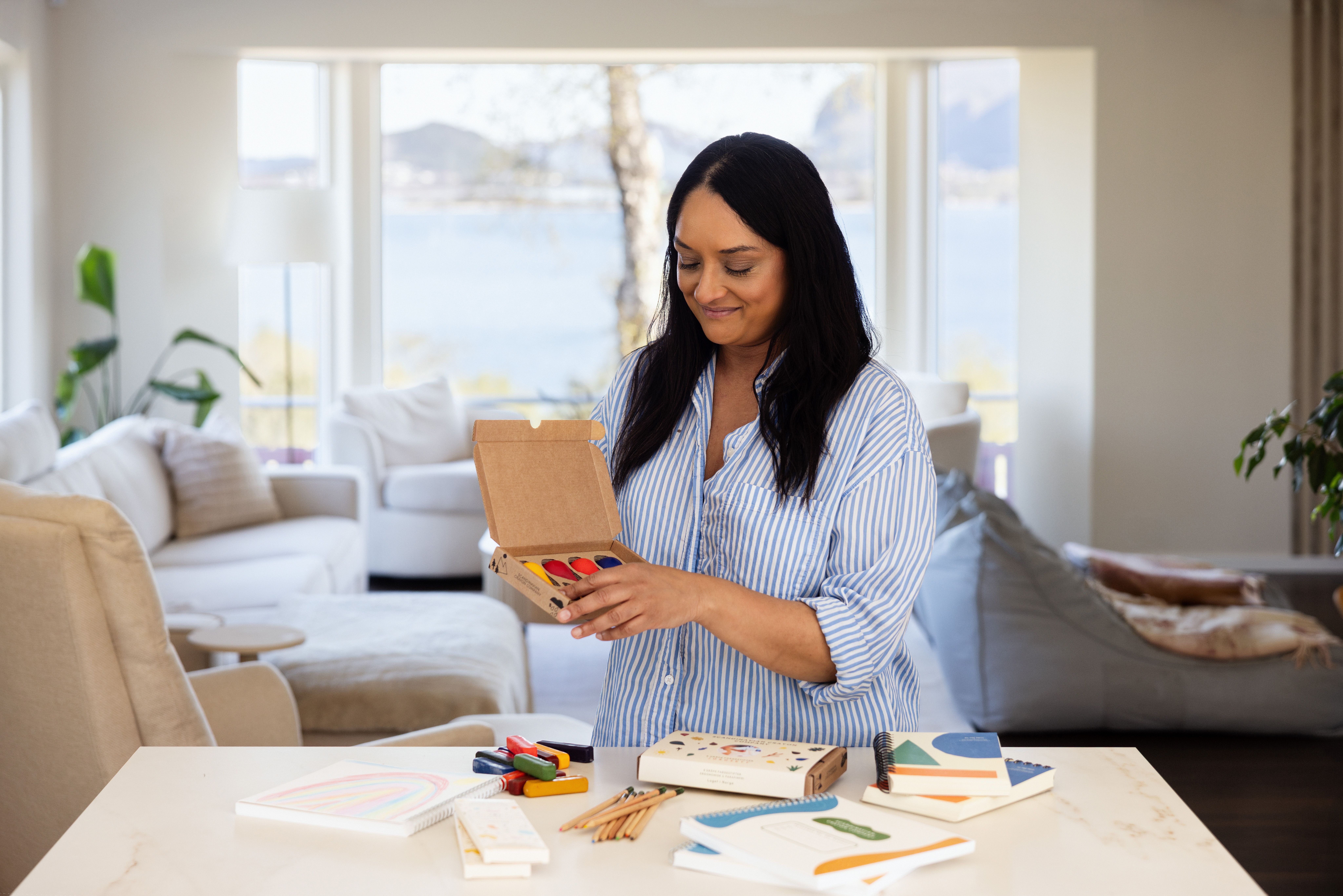 Kvinne sitter ved et bord med fargestifter og tegneutstyr fra Scandinavian Crayon Company. Produktene er utviklet med fokus på kreativ lek og bærekraftige materialer for barn.