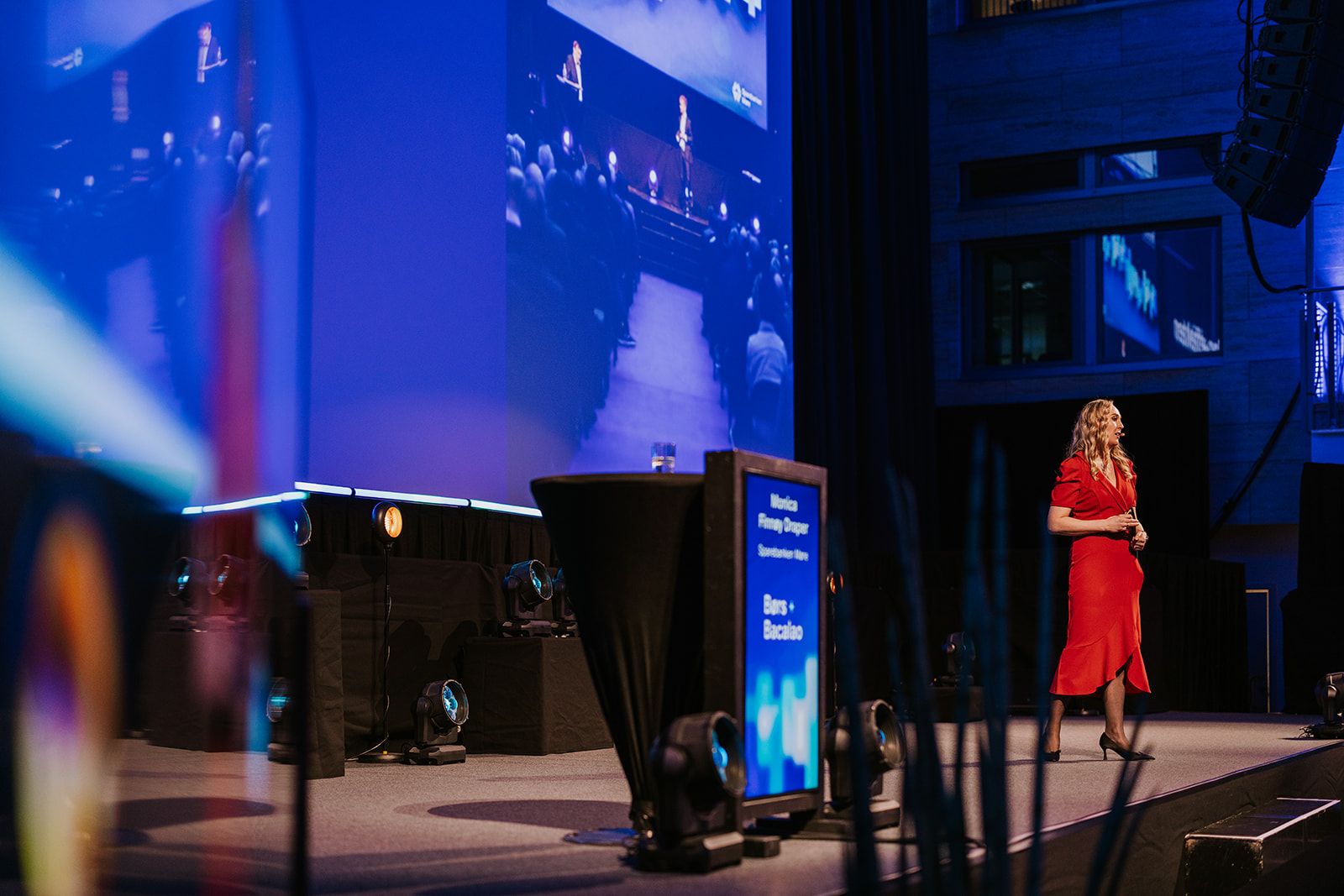 Kvinne med rød kjole, står på en scene og presenterer. 
