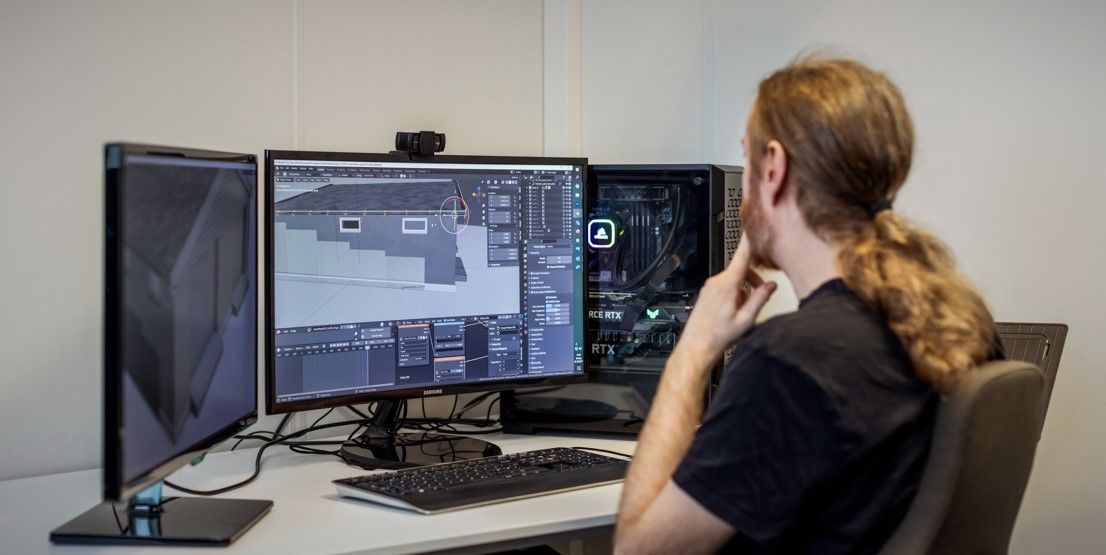 Ansatt sitter foran flere dataskjermer og arbeider med digitale modeller og grafikk på kontor hos Spesialistbedriften.