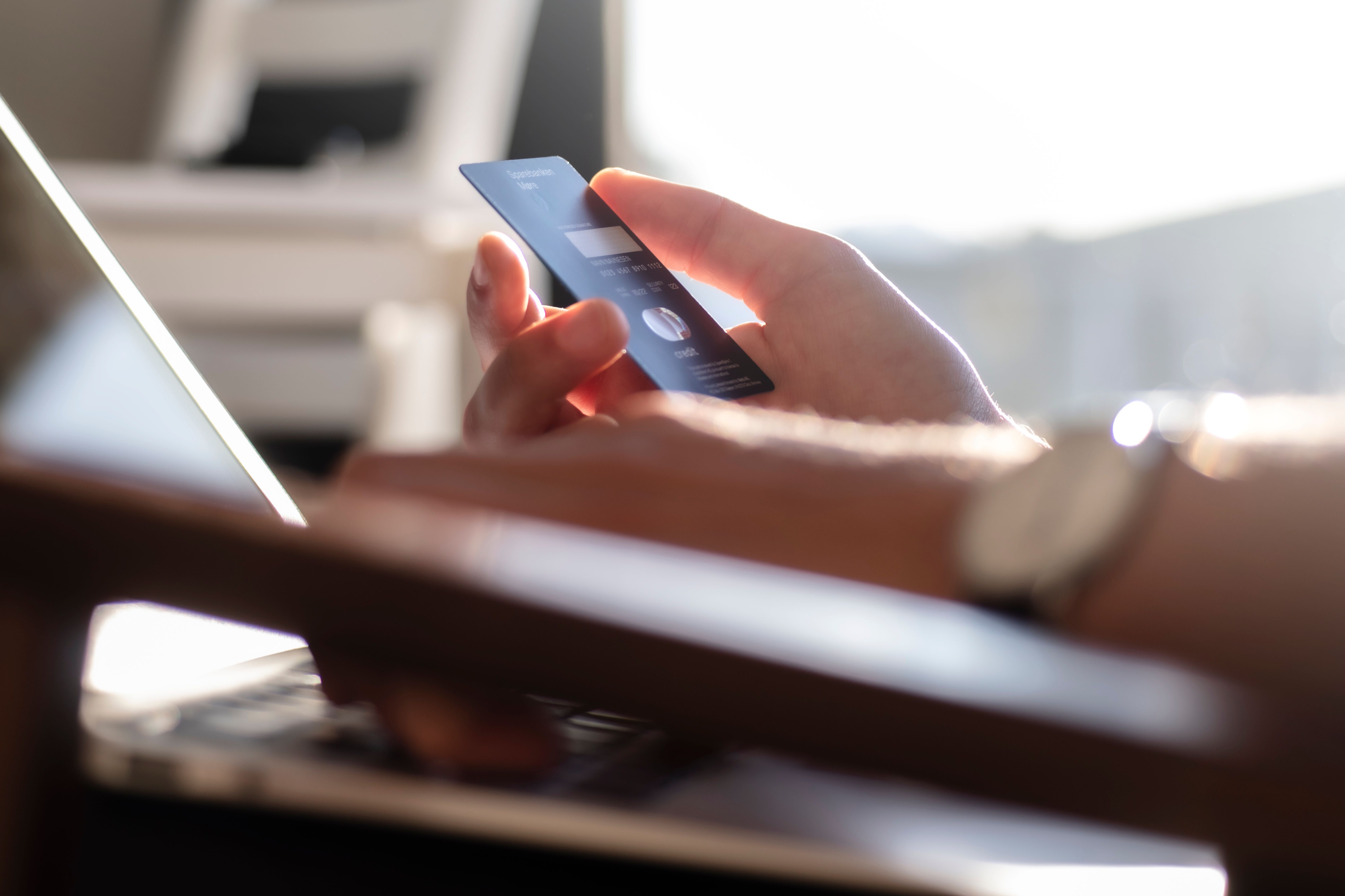 Mørkeblått kredittkort holdes i en hånd fremfor en PC-skjerm