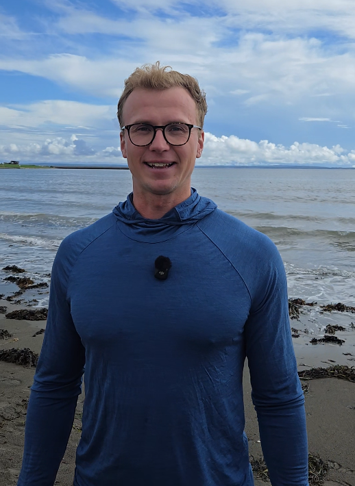 Mann med sjø og fjøre i bakgrunn. 