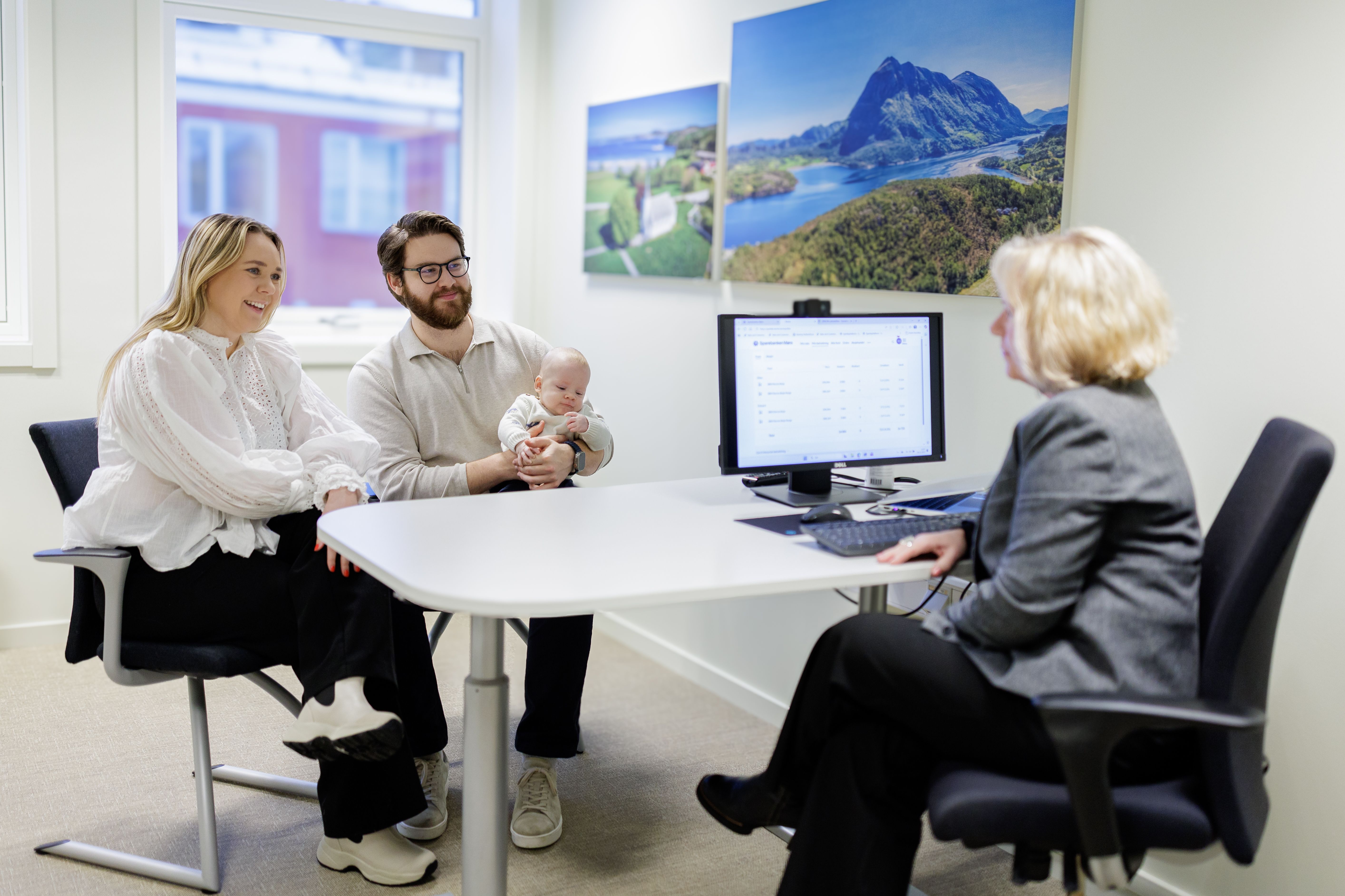 Ungt par med baby på hånden i møte med bankrådgiver, i bankens lokaler 